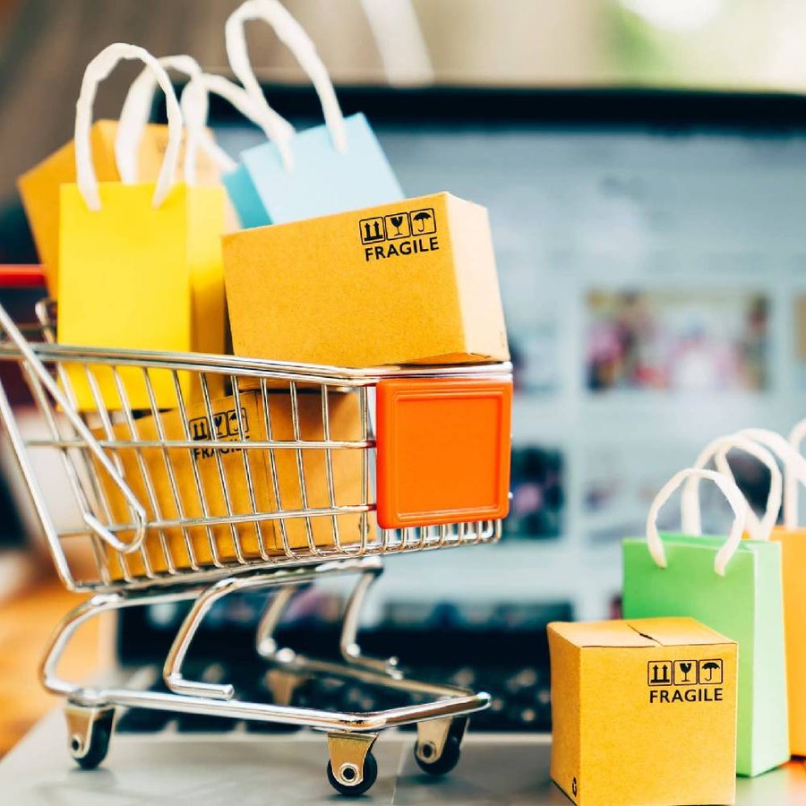 A shopping cart filled with colorful bags beside a laptop