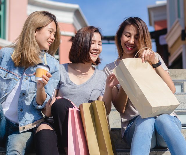 Three friends sitting on steps with shopping bags